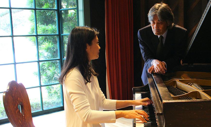 woman plays grand piano while man is overlooking