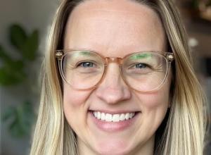 Close up of a woman smiling with blonde hair and glasses.
