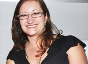 Female with long brown hair, wearing glasses and a black top.